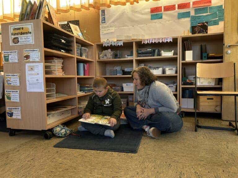 Eine Frau und ein Kind sitzen auf dem Boden in einem Klassenzimmer und lesen gemeinsam.