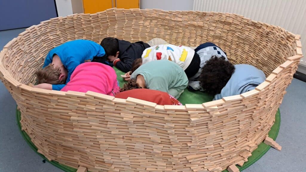 Kinder liegen in selbst gebautem Korb aus Holzstäbchen